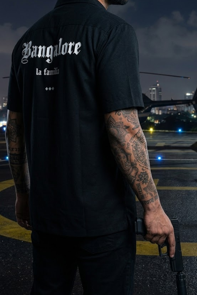 Person wearing a black shirt with 'Bangalore la familia' text, standing in an urban setting at night.
